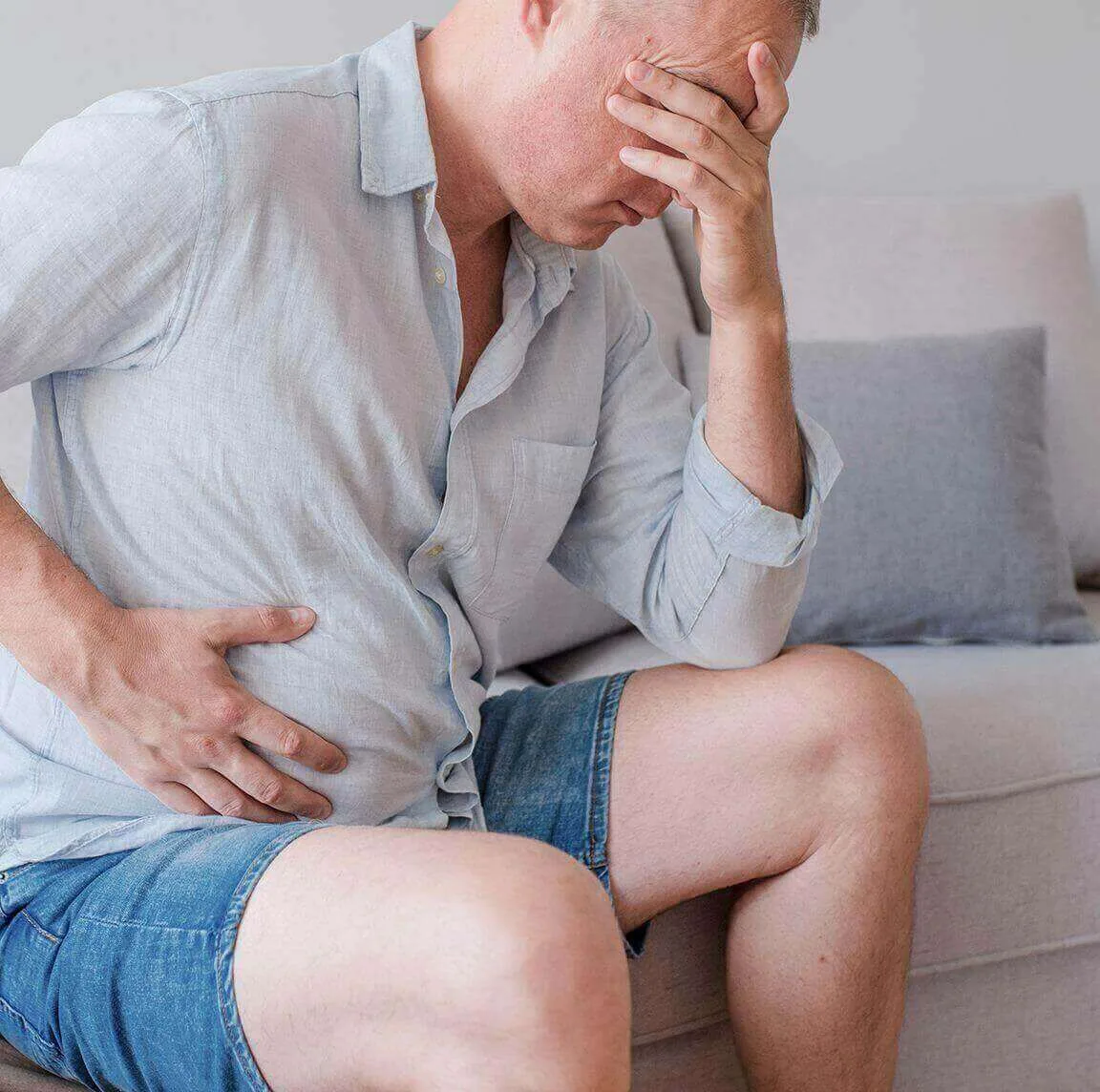 A man holding his face and stomach, looking distressed and experiencing faecal incontinence