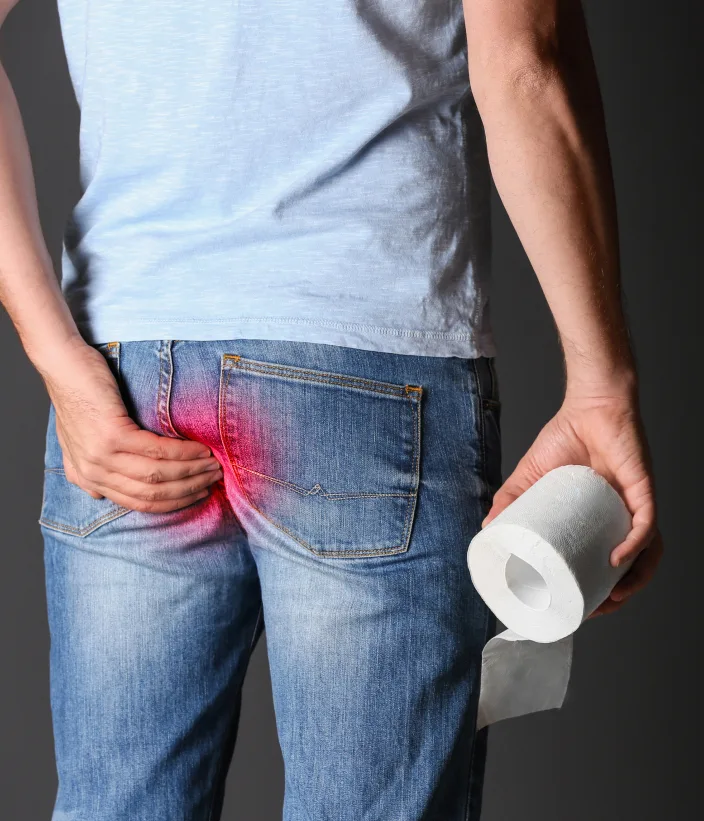 A person holding a toilet paper roll with a hand on their lower buttocks, showing physical discomfort.