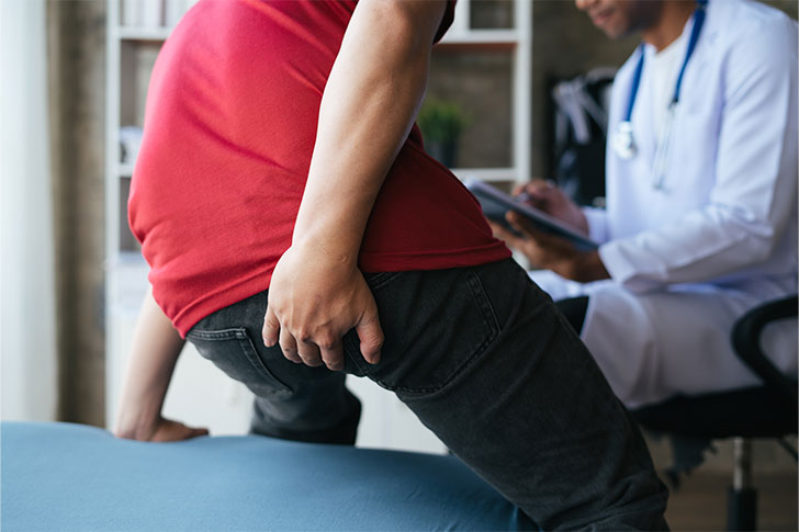 A man clutching his buttocks while consulting a medical professional
