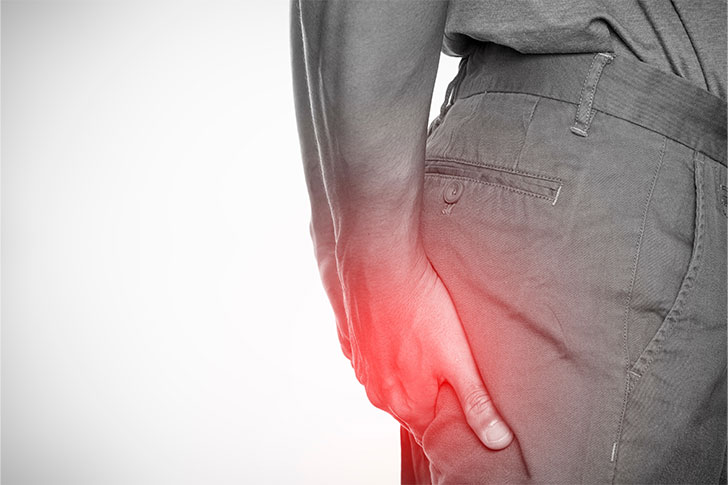 A man clutching his buttocks with a soft red glow indicating pain or discomfort